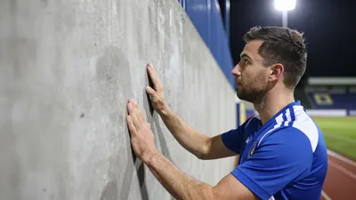 A Barrow AFC ground staff member in a blue and white kit inspecting a concrete wall at Holker Street