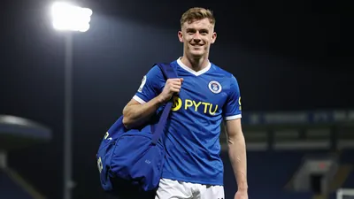 A photorealistic image of an anonymous 22-year-old Barrow AFC player, wearing a blue jersey and white shorts, with a blue...