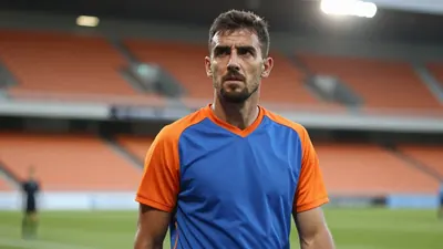 A medium shot of a 25-year-old male coach with a rugged build, dressed in a plain blue and orange jersey made of a...