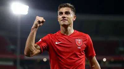 Photorealistic shot of a 28-year-old midfielder in a solid red shirt, celebrating his signing with a fist pump
