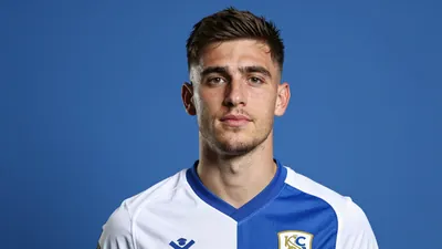 A photorealistic image of an anonymous 26-year-old midfielder in a Barrow Football Club jersey, with a confident...