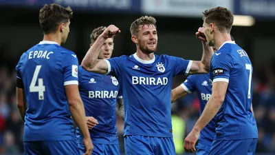 A 25-year-old Barrow player, wearing a blue jersey, celebrates a goal with his teammates, photographed with an 85mm f/1.4...