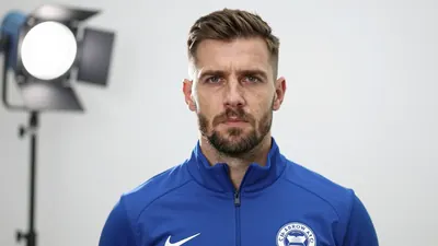 A close-up shot of a Barrow AFC staff member in a blue tracksuit, with a serious expression, standing in front of a white...