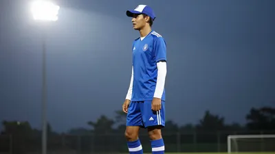 A 23-year-old left-sided defender in a blue jersey with white sleeves, wearing a blue and white striped sock, and a blue...