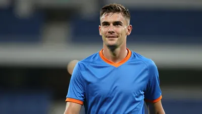 Mid-30s Barrow forward, athletic build, waist-up, wearing a plain blue jersey with orange trim, soft cotton texture;