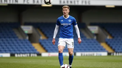 A tight action crop of an anonymous Barrow AFC player in a blue shirt with white sleeves and white shorts, with a white...