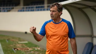 A 50-year-old, ruggedly-built man in his mid-50s, dressed in a plain, unmarked blue and orange jersey made of...