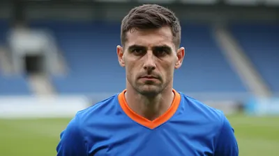 Mid-30s Barrow manager, athletic build, waist-up, intense gaze, short dark hair, slight stubble, wearing a plain blue...