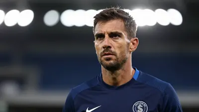 A mid-30s male coach in a navy blue Barrow training shirt, head-and-shoulders shot, intense expression, background...