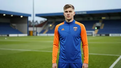 A determined 25-year-old Barrow midfielder, athletic build, in a plain blue and orange training top, stands on the SO...