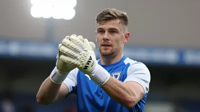 A tight action crop of Barrow AFC's goalkeeper, a young man with a strong build, aged 22-25, wearing a blue jersey with...