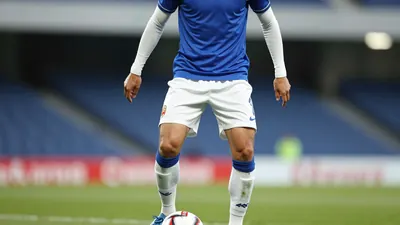 A photorealistic image of an anonymous Barrow player in a blue jersey with white sleeves and white shorts, taken with a...