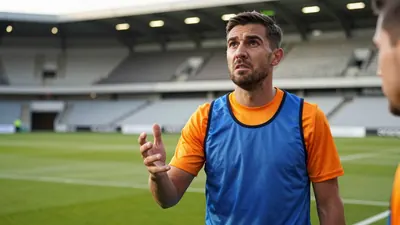 A 35-year-old, 5'10" Barrow midfielder, wearing a plain, unmarked blue and orange polyester training top, looks up from...