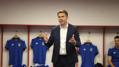 A Barrow AFC manager in his mid-40s, wearing a navy blue suit with a white shirt, delivering a passionate speech to the...