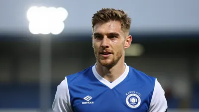 A close-up shot of a Barrow AFC player in a blue jersey with white sleeves, looking determined as they prepare to take on...